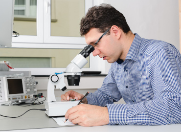 Friedrich Mäckle schaut in ein Mikroskop und macht sich Notizen